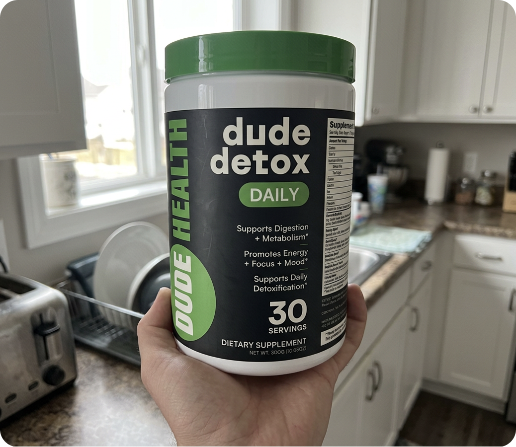 Hand holding Dude Detox DAILY in a kitchen